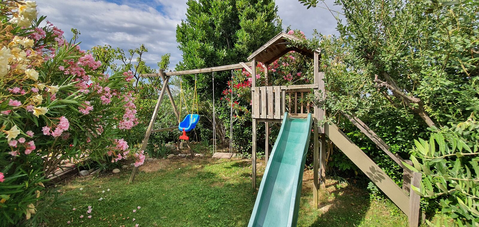 Aire de jeux pour enfants avec toboggan et balançoire au milieu des lauriers